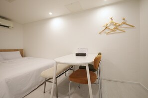 Una habitación de hotel con una cama, una mesita, una silla y un perchero en la pared.