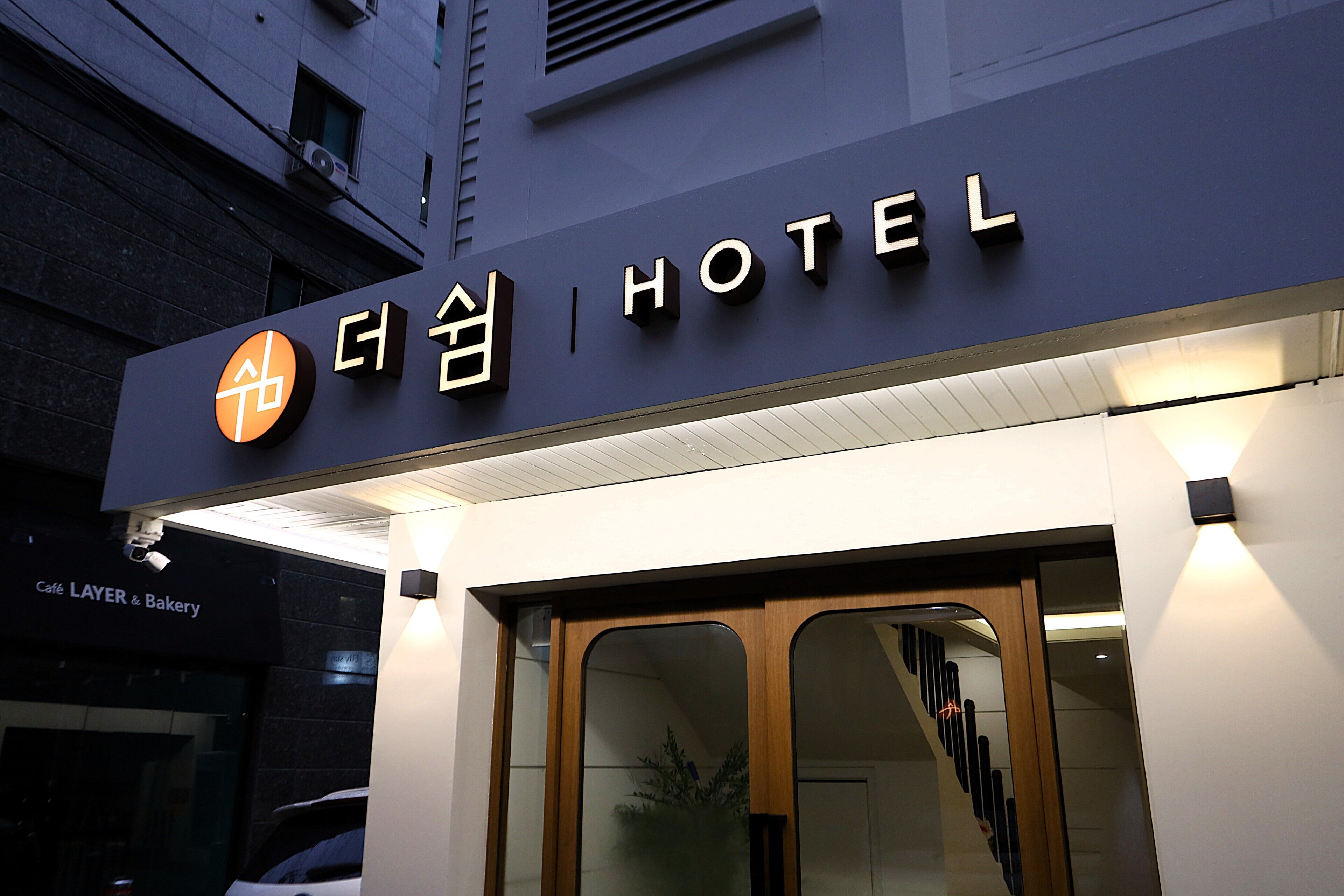 Entrada de um hotel com uma placa que inclui caracteres coreanos e a palavra 'HOTEL'.