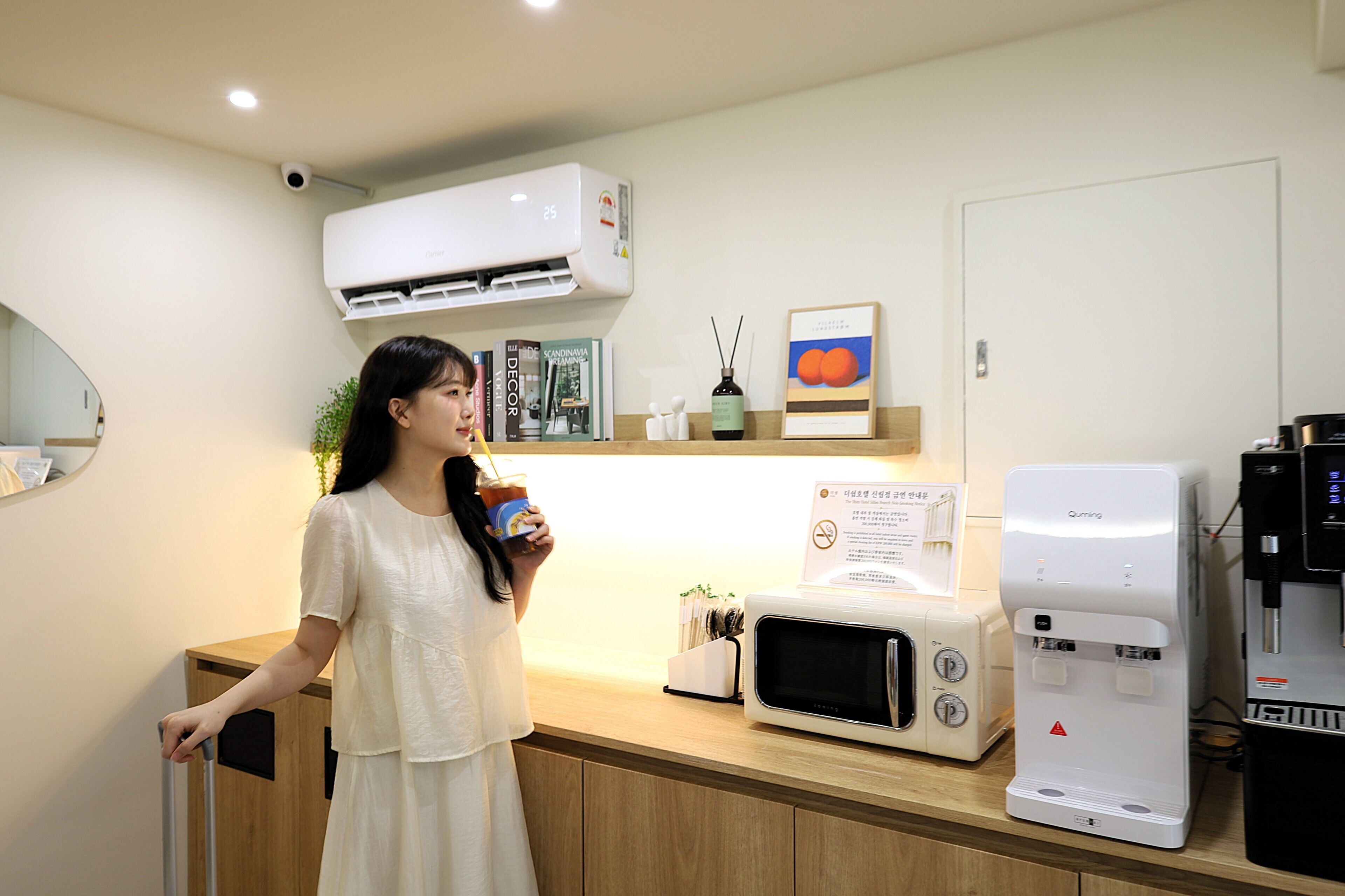 A person standing in a room with a coffee machine, a microwave, and a shelf with books and a framed picture.