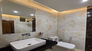 A bathroom with a large mirror, a white sink, and a white bathtub. - Hotel Narayana Palace (Khajuraho)