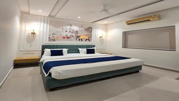 A modern bedroom with a large bed, a wall-mounted air conditioner, and a decorative mural. - Hotel Narayana Palace (Khajuraho)