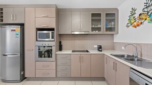 A modern kitchen with stainless steel appliances, a microwave, oven, and a sink with a faucet. - Palm Cove One-Bedroom Apartment with Pool | Myrtle at Oliva (Palm Cove)