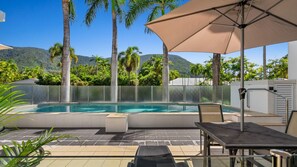 A swimming pool with a glass enclosure, surrounded by palm trees and a mountain backdrop. - Palm Cove One-Bedroom Apartment with Pool | Oliva Breeze Apartment (Palm Cove)