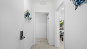 A hallway with a door leading to a room, a wall-mounted decorative piece, and a glimpse of a dining area with a table and chairs. - Palm Cove One-Bedroom Apartment with Pool | Myrtle at Oliva (Palm Cove)