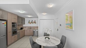 A modern kitchen with built-in appliances, a dining area with a marble table, and a wall-mounted artwork. - Palm Cove One-Bedroom Apartment with Pool | Oliva Breeze Apartment (Palm Cove)