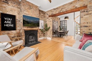 A living room with a fireplace, a television mounted on the wall, and a dining area with a table and chairs. - Newly renovated 2 Bdrm Terrace + Rooftop (City of Sydney)