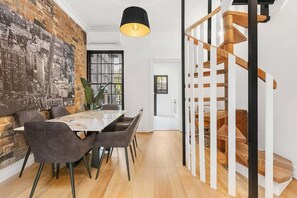 A dining area with a brick wall, a cityscape mural, and a staircase with wooden steps and white railings. - Newly renovated 2 Bdrm Terrace + Rooftop (City of Sydney)