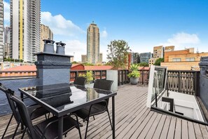 A rooftop terrace with a glass table and chairs, surrounded by a wooden deck and city views. - Newly renovated 2 Bdrm Terrace + Rooftop (City of Sydney)