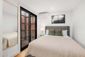 A bedroom with a bed, a nightstand, a lamp, a picture on the wall, and a sliding door to a balcony. - Newly renovated 2 Bdrm Terrace + Rooftop (City of Sydney)