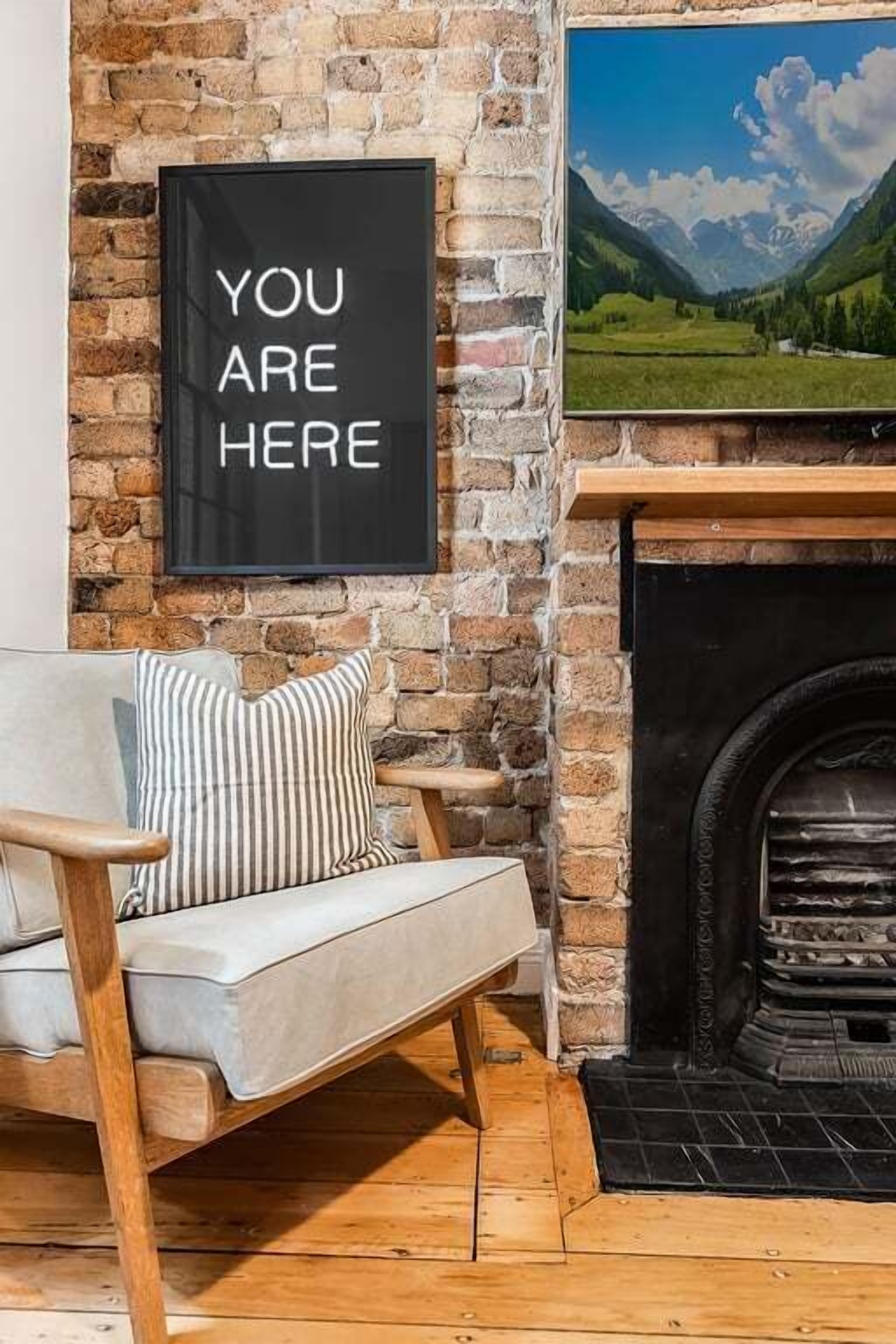 Ein gemütliches Zimmer mit Kamin, einem gerahmten Motivationsspruch und einer Couch mit gestreiften Kissen.