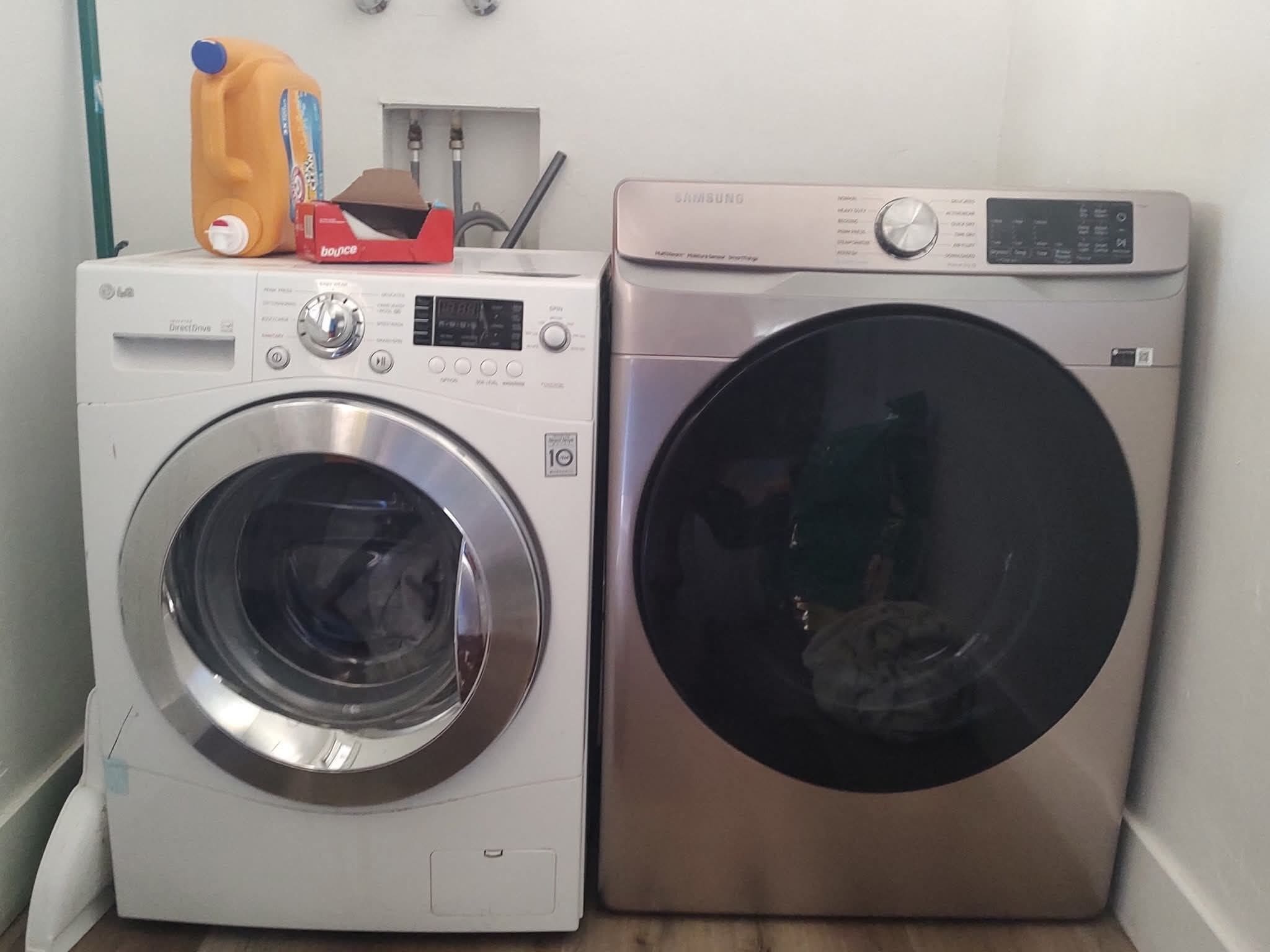 Two front-loading washing machines, one white and one silver, with a hose and a bottle on top.