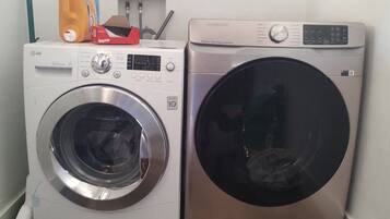 Two front-loading washing machines, one white and one silver, with a hose and a bottle on top.