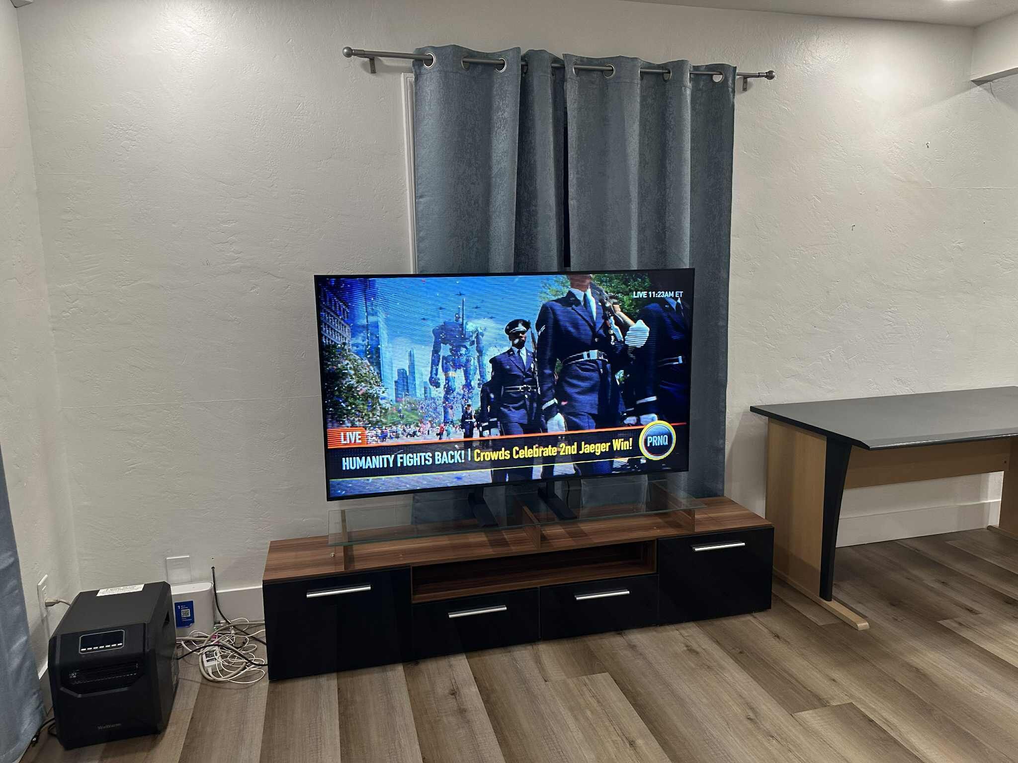 A flat-screen TV mounted on a wooden entertainment unit with a curtain above it.