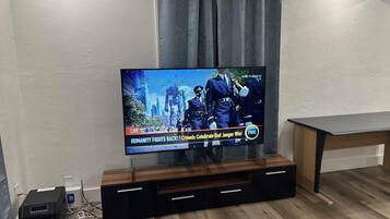 A flat-screen TV mounted on a wooden entertainment unit with a curtain above it.