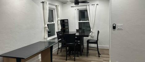 Een gezellig eetgedeelte met een tafel, stoelen, een plafondventilator en een raam met gordijnen.