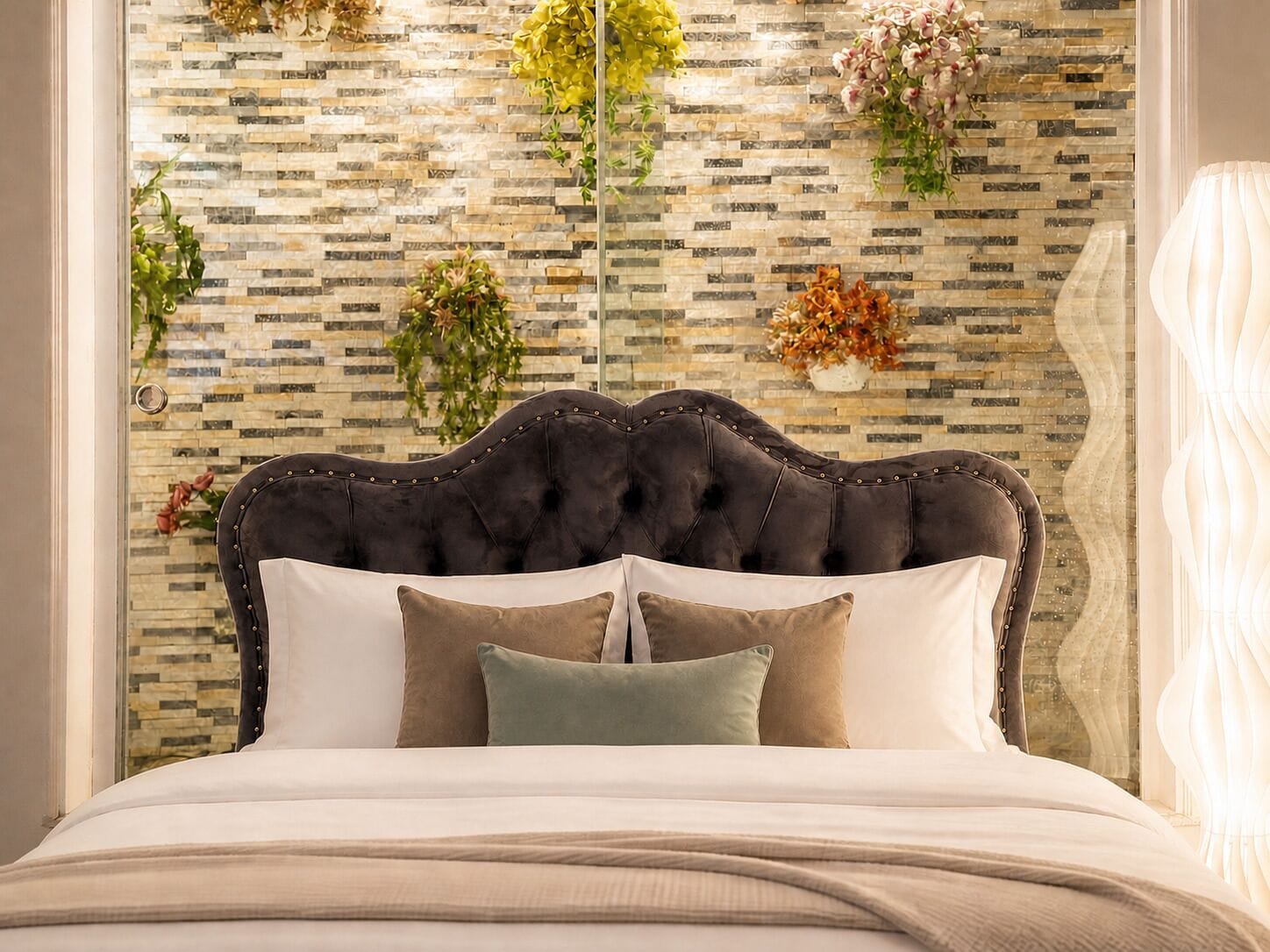 A bed with a tufted headboard, multiple pillows, and a decorative wall with a mosaic pattern.