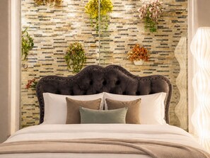 Een bed met een gestoffeerd hoofdbord, meerdere kussens en een decoratieve muur met een mozaïekpatroon.