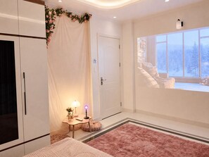 Un dormitorio con cama, mesita de noche, lámpara, ventana que ofrece vistas a árboles cubiertos de nieve, y una puerta con letrero de no fumar.