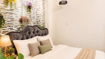 Een slaapkamer met een gestoffeerd hoofdeinde, een bed met witte lakens, een lamp en decoratieve planten.