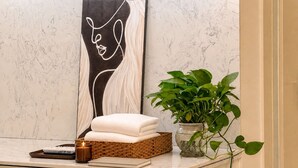 Un baño con pared de mármol, una pila de toallas, una cesta, una vela, un control remoto y una planta en maceta.