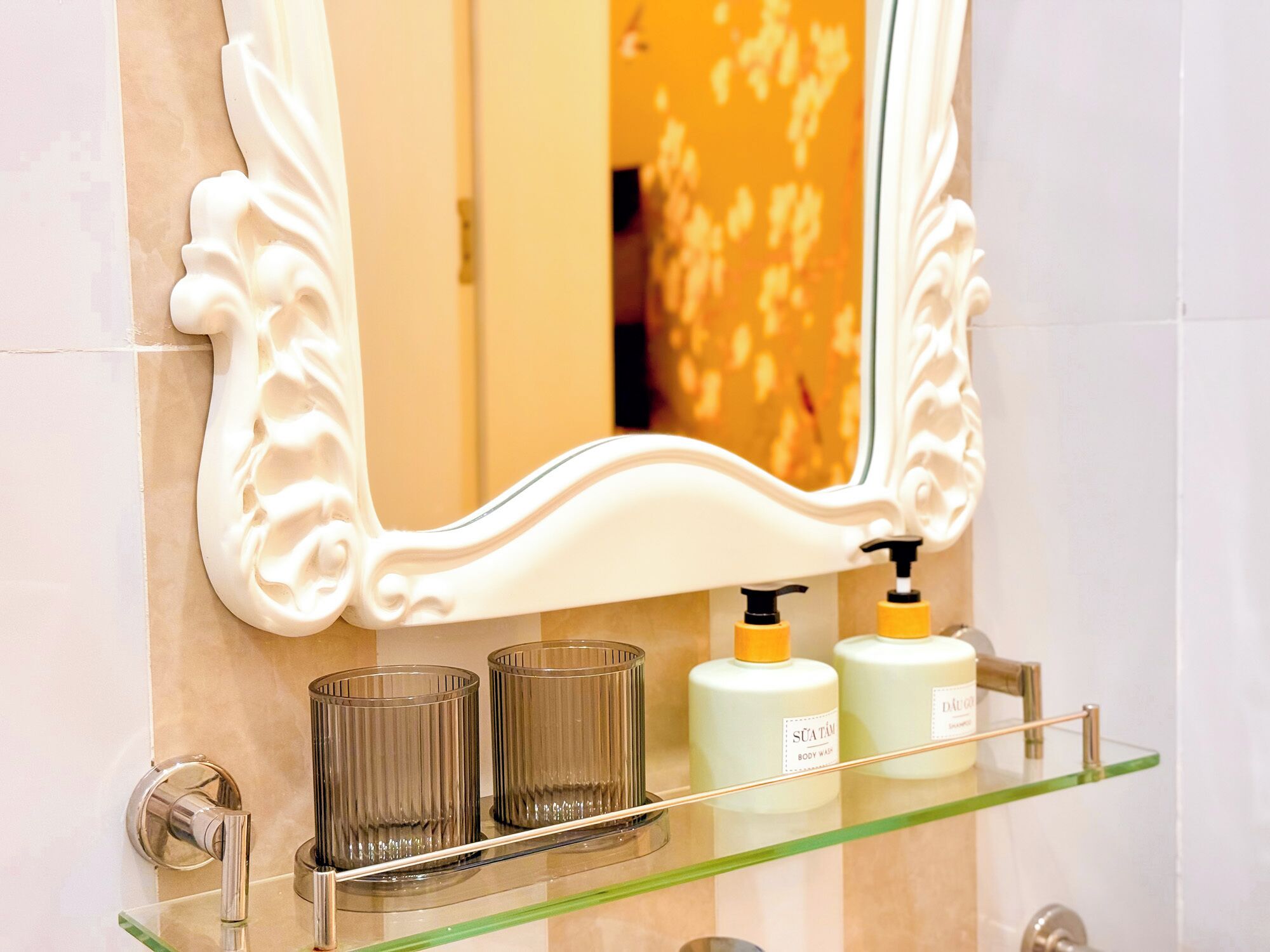A bathroom with a mirror, two glass bottles, and a glass shelf.