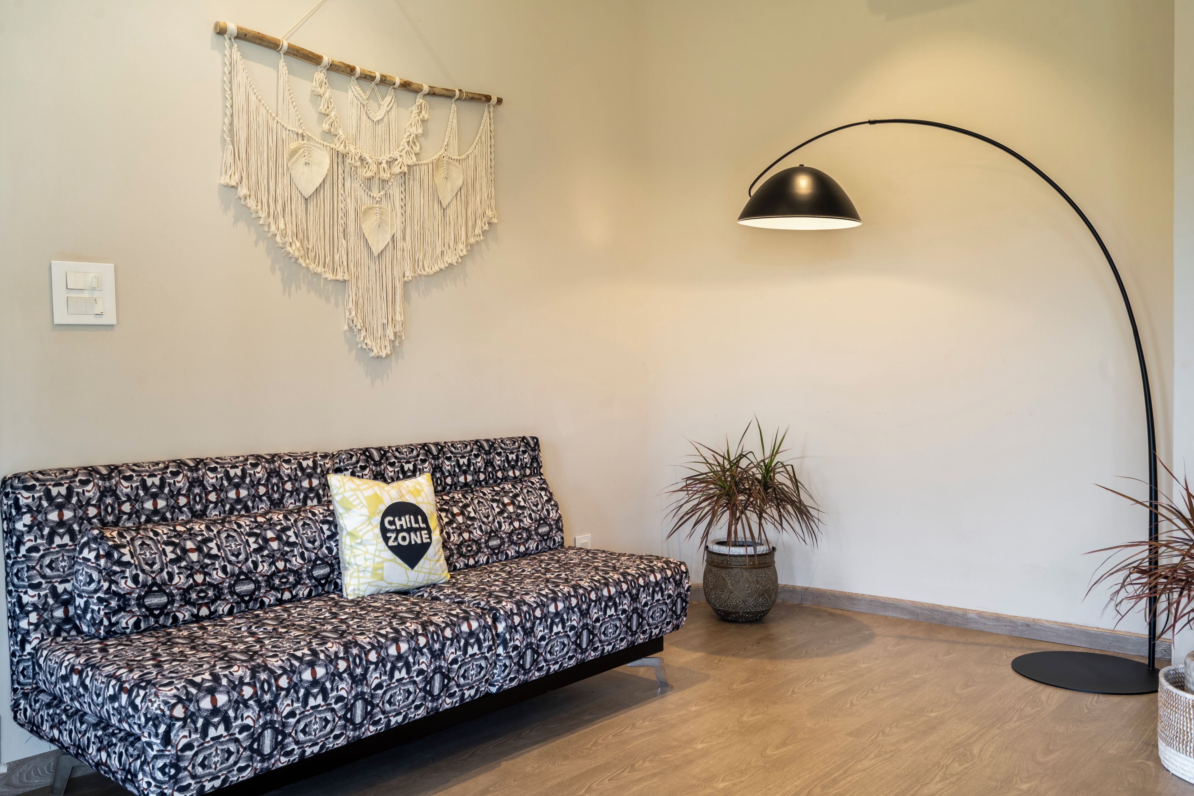 Een moderne woonkamer met een gestreept sofa, een macramé wanddecoratie, een vloerlamp en een potplant.