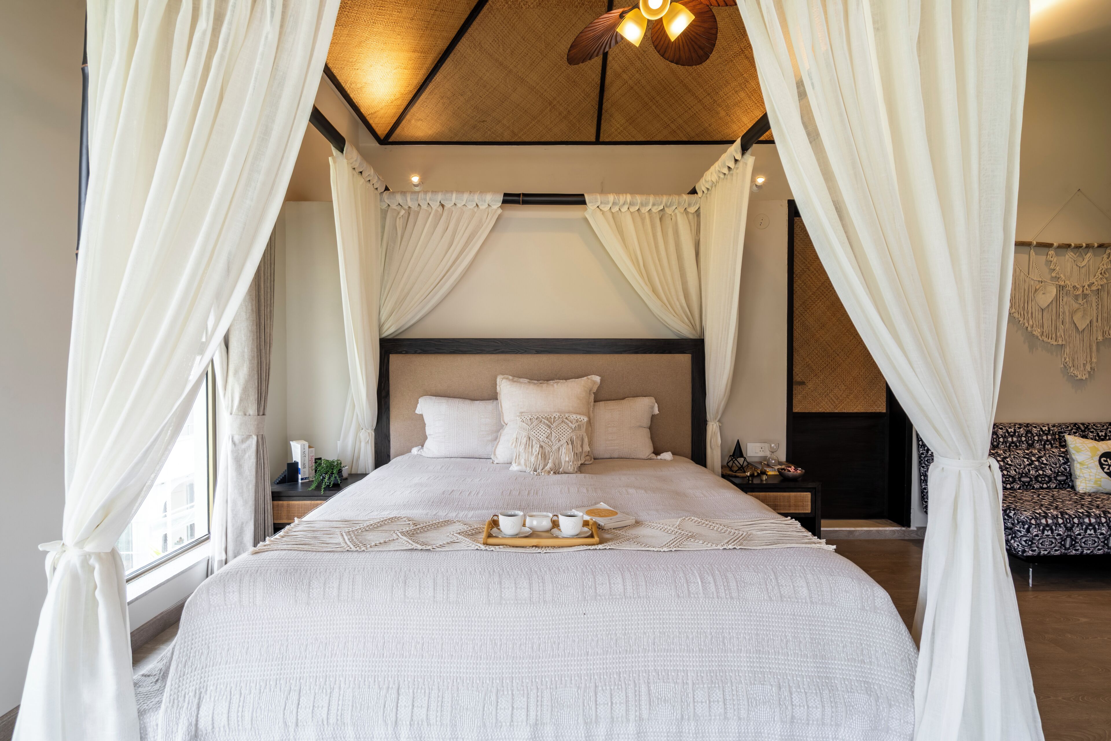 A bedroom with a canopy bed, a bedside table with a bowl of fruit, and a wall-mounted macrame decoration.