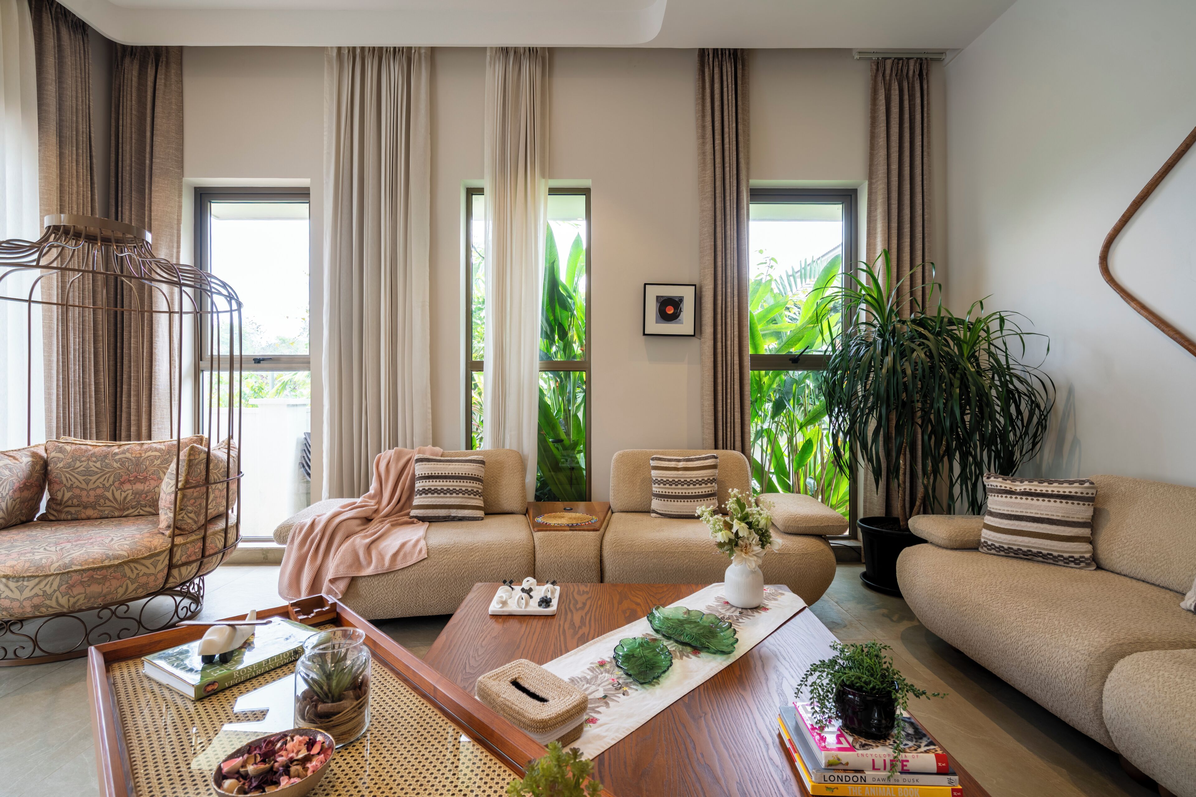 A living room with a sofa set, a coffee table with decorative items, and a view of greenery outside.