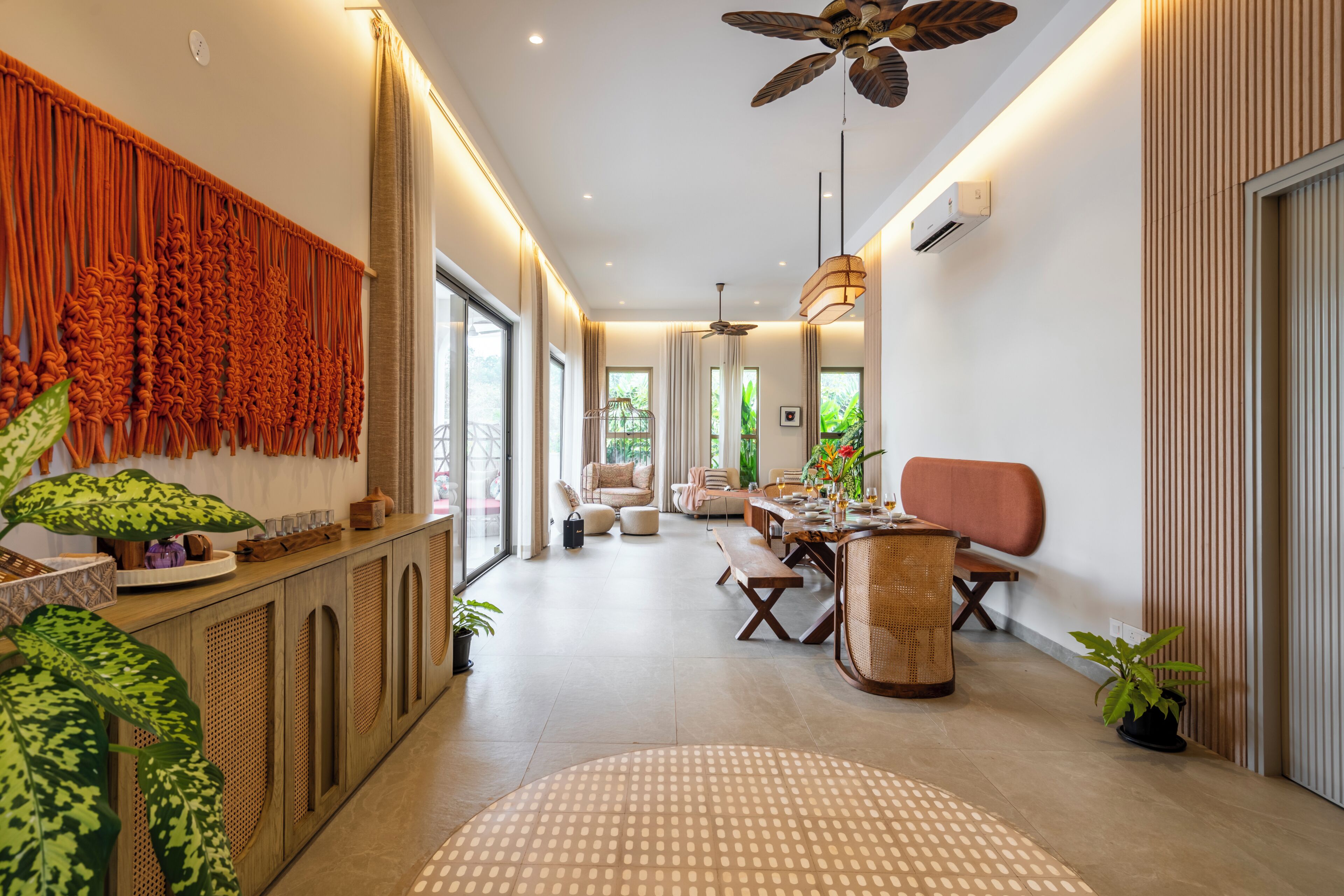 Un interior moderno con un largo pasillo que conduce a un comedor, con ventilador de techo, ventanas amplias y diversas opciones de asientos.