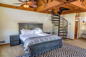 Een slaapkamer met een bed, nachtkastje, kaptafel, wenteltrap en plafondventilator.