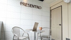 Ein modernes Interieur mit einer weißen Ziegelwand, einer Tür und zwei Metallstühlen um einen Tisch mit einem Laptop und einem Getränk.