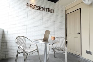 Ein modernes Interieur mit einer weißen Ziegelwand, einer Tür und zwei Metallstühlen um einen Tisch mit einem Laptop und einem Getränk.