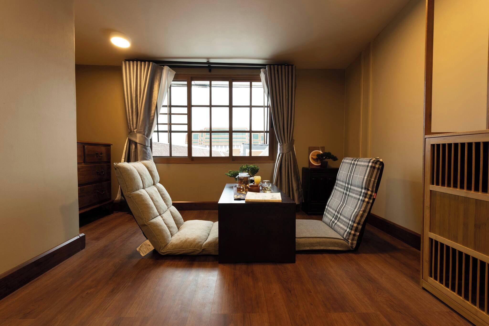 A room with a wooden floor, a sofa, a chair, a small table with a plant, and a window with curtains.