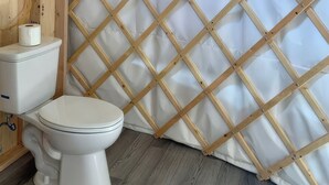 A toilet with a white lid, a roll of toilet paper, and a wooden lattice partition in a bathroom. - A tranquil yurt with all the amenities in charming Big Lake (Big Lake)