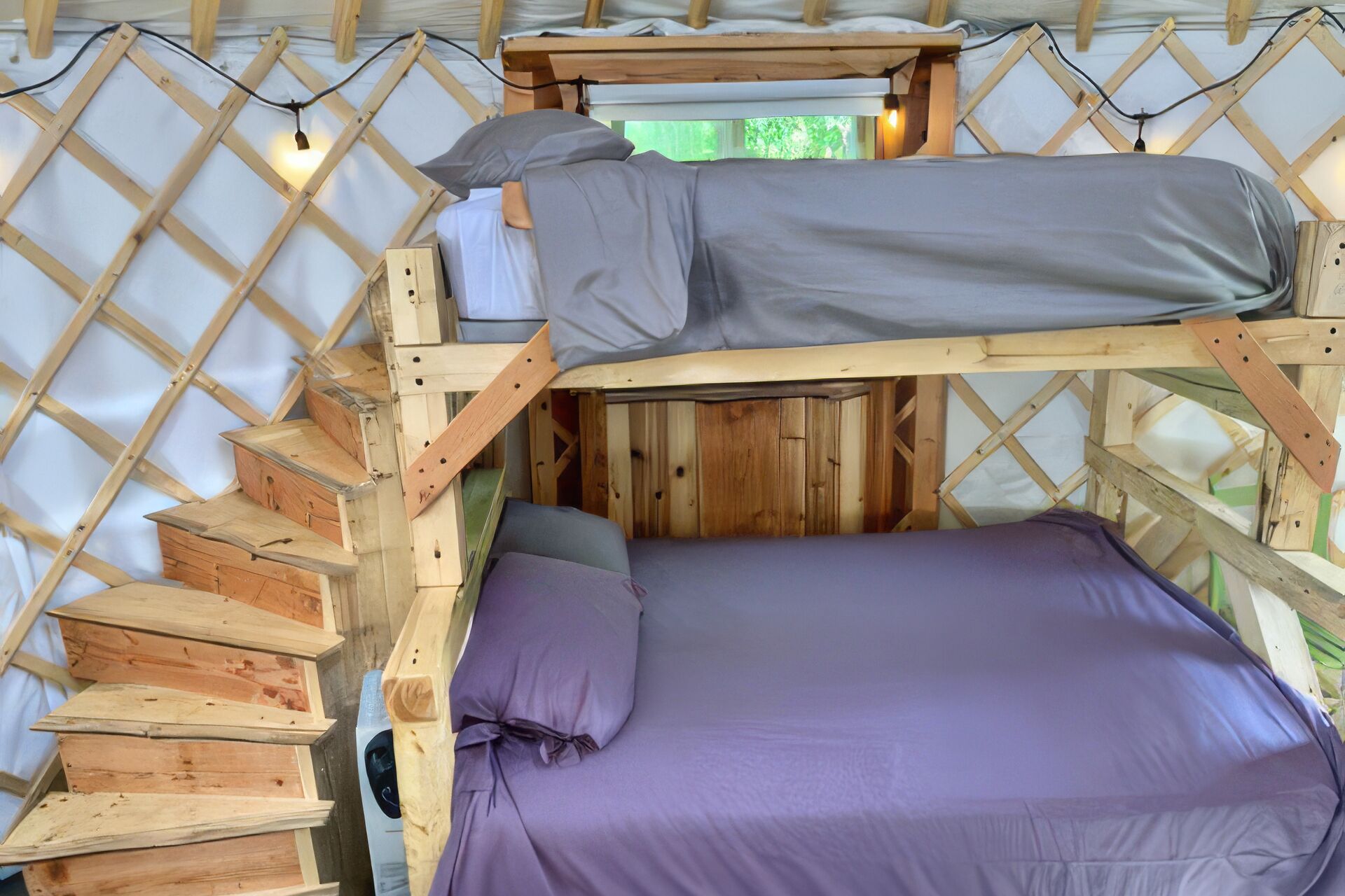 A bunk bed with a mattress and pillows, wooden steps, and a lattice wall.
