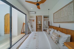 Un dormitorio con una cama grande, un ventilador de techo, un armario y vistas a través de un ventanal.