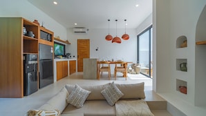 A modern kitchen with a built-in oven, a refrigerator, and a microwave. There is a dining area with a wooden table and chairs. - Villa Rame (Uluwatu)