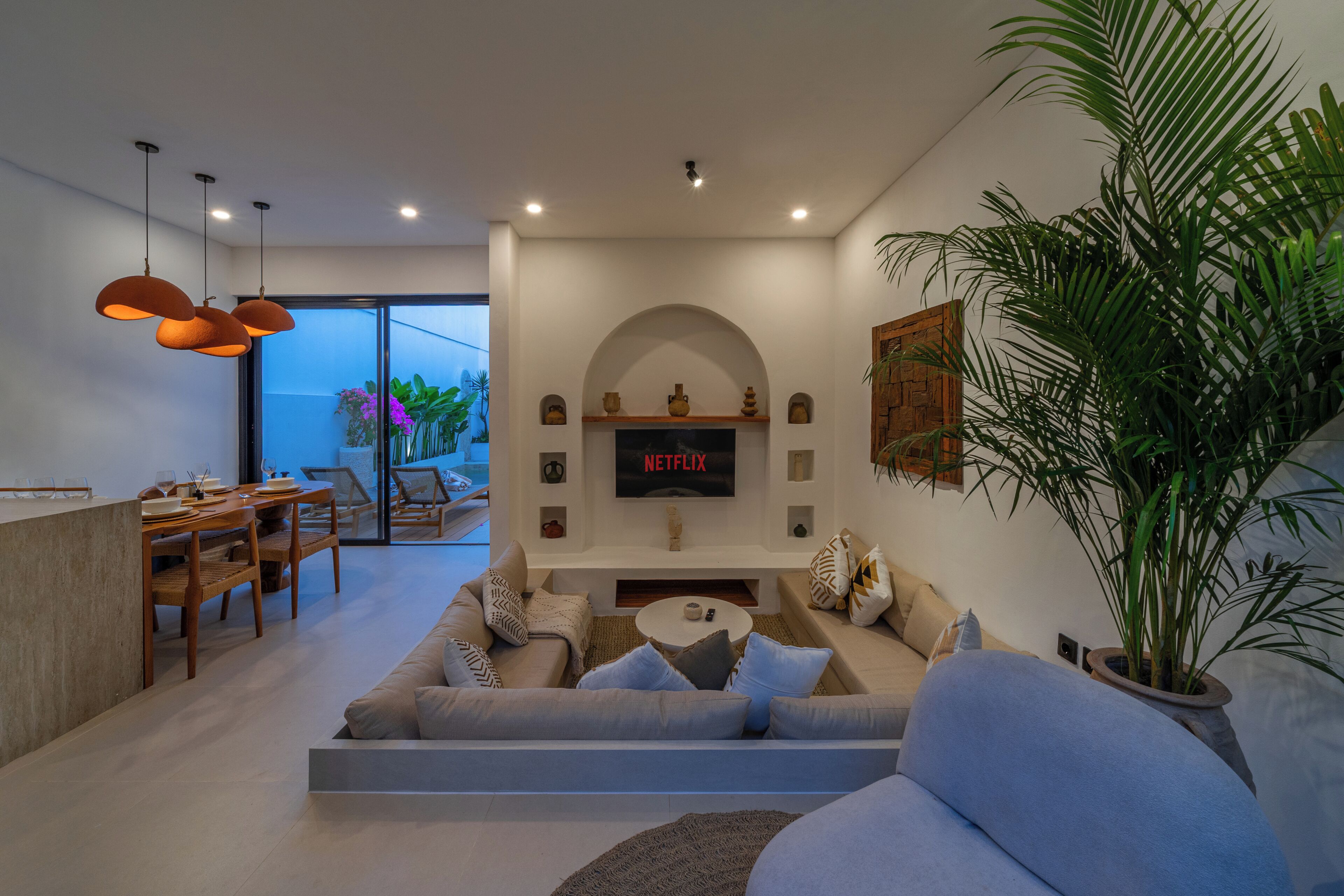 Una sala moderna con un sofá, un televisor montado en la pared y una zona de comedor con sillas y una mesa.
