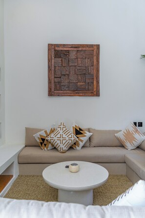 Ein modernes Wohnzimmer mit einem beigefarbenen Sofa, gemusterten Kissen, einem runden Couchtisch und einer rustikalen Holztischlerei an der Wand.