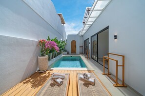 Un área de piscina privada con terraza de madera, sillas de descanso y una planta en maceta.