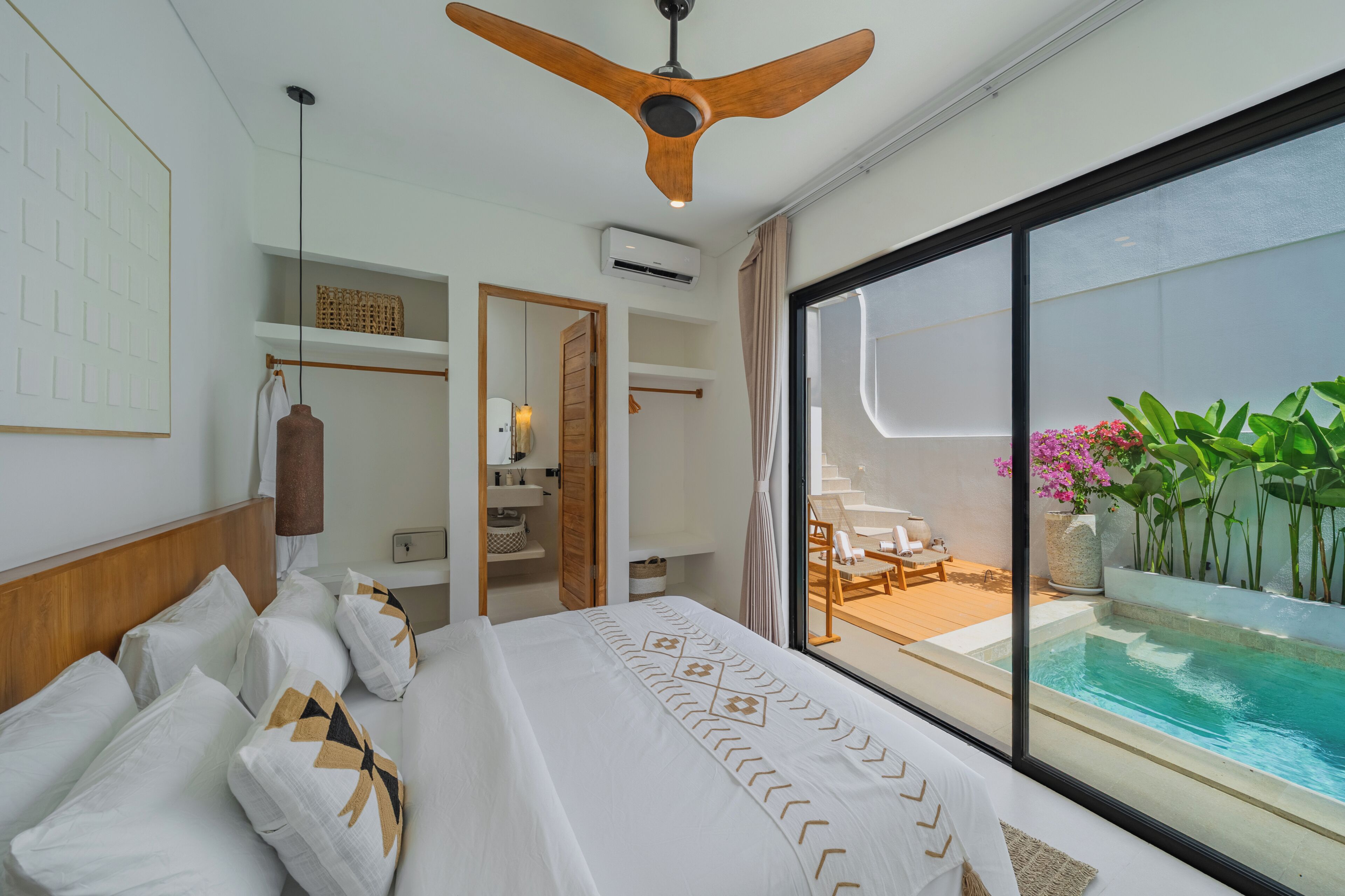 Une chambre dotée d’un grand lit, d’un ventilateur de plafond, d’une salle de bain et offrant une vue sur une piscine.