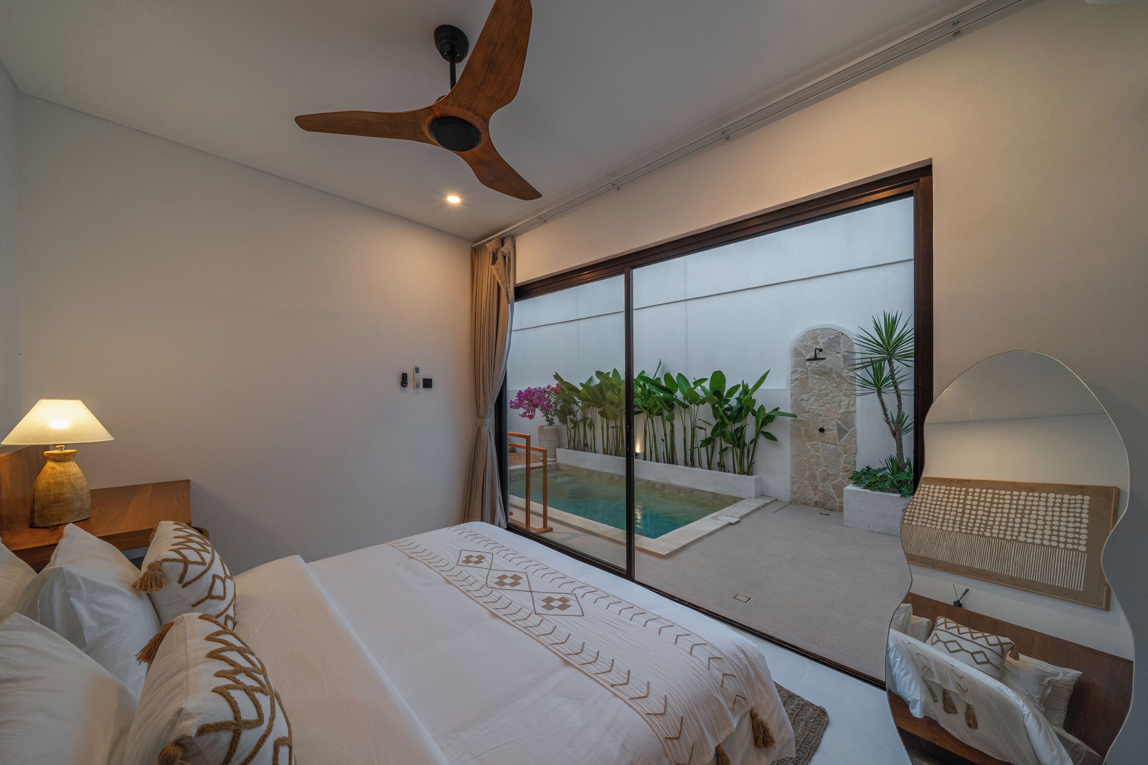 Une chambre d’hôtel avec un lit, un ventilateur de plafond, une vue sur la piscine et une salle de bain avec un miroir.