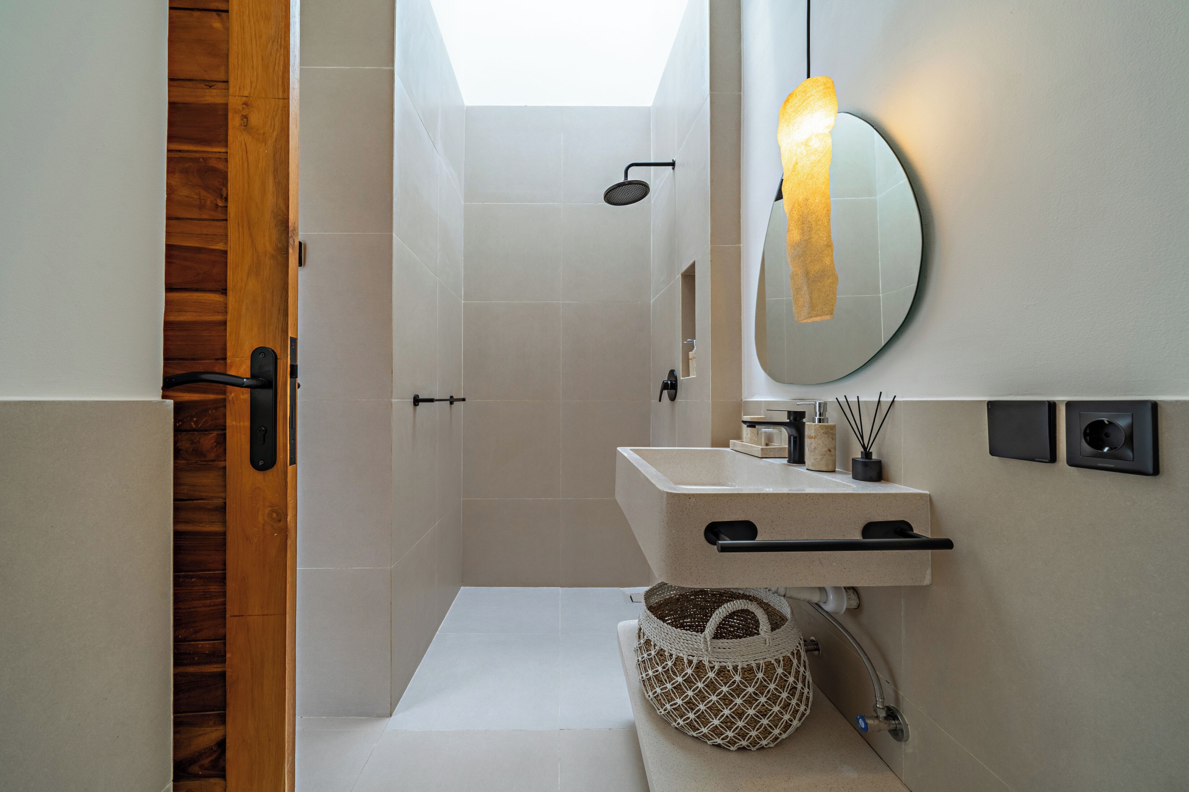 Un baño moderno con puerta de madera, ducha, lavamanos con toallero y espejo con luz.