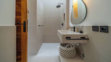 Un baño moderno con puerta de madera, ducha, lavamanos con toallero y espejo con luz.