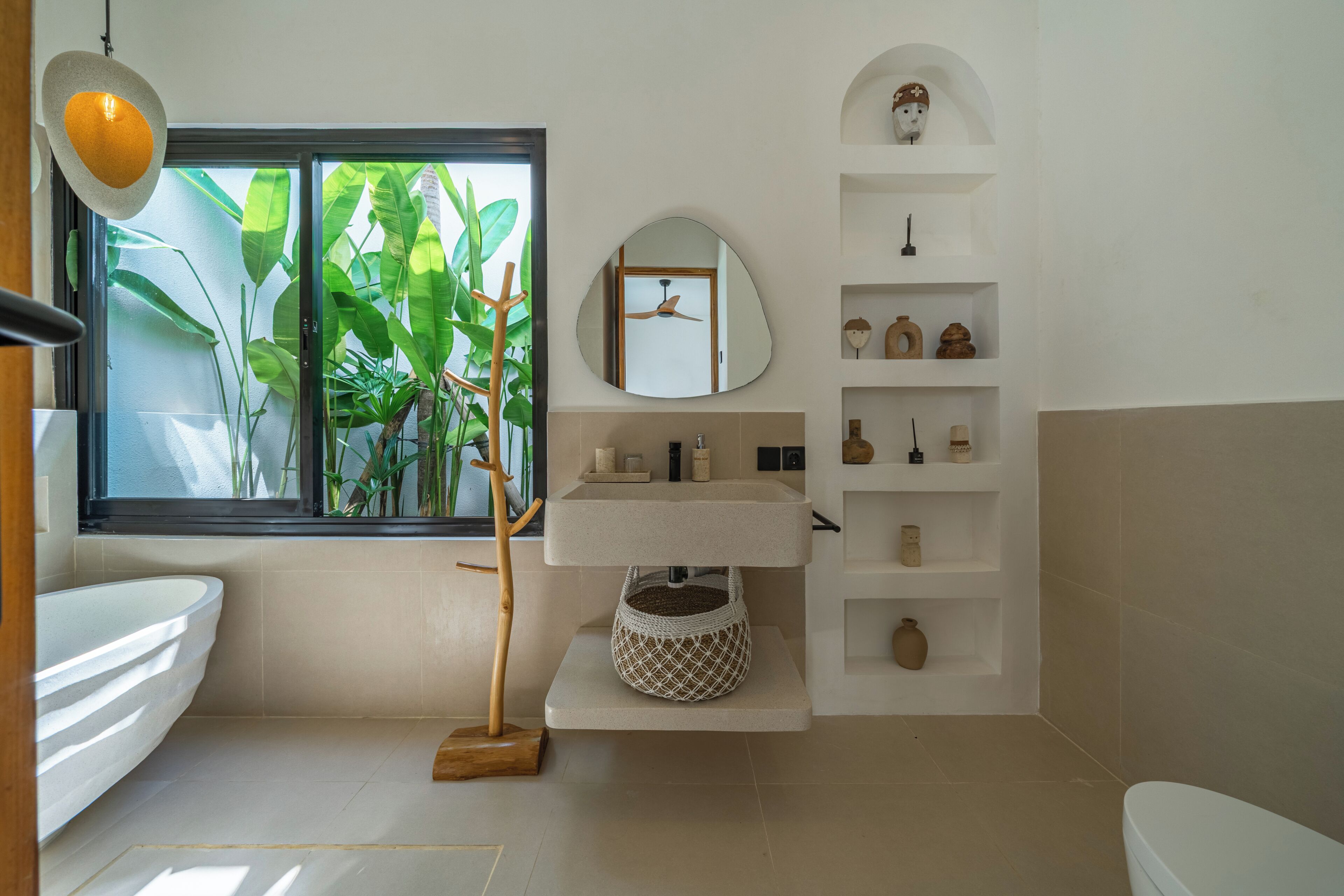 Une salle de bain dotée d’une grande fenêtre, d’un lavabo, d’un miroir et d’étagères où sont disposés des objets décoratifs.