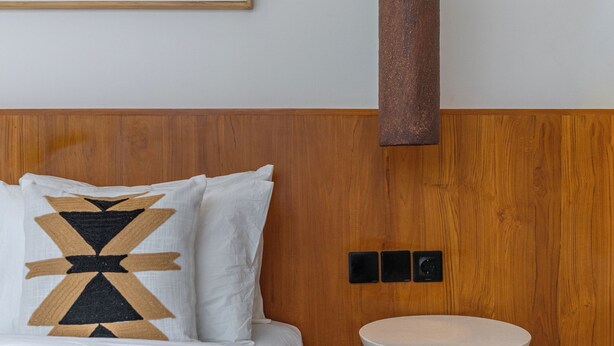 A neatly arranged bedroom with a bed, pillows, a bedside table, a wall-mounted light fixture, and a framed artwork. - Villa Rame (Uluwatu)