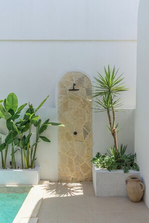 Un arco de piedra que da paso a una zona de piscina con plantas en macetas y una maceta de terracota.