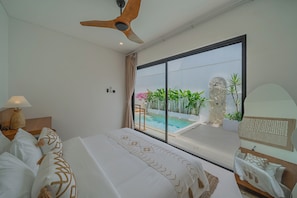 A hotel room with a large bed, a ceiling fan, a view of a pool, and a stone wall. - Villa Rame (Uluwatu)