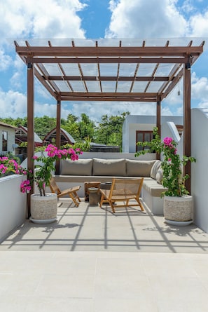 A covered outdoor seating area with a sofa, two wicker chairs, and two potted plants with pink flowers. - Villa Rame (Uluwatu)