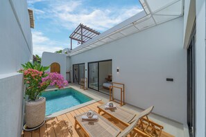 A modern outdoor pool area with a wooden deck, lounge chairs, and a potted plant.